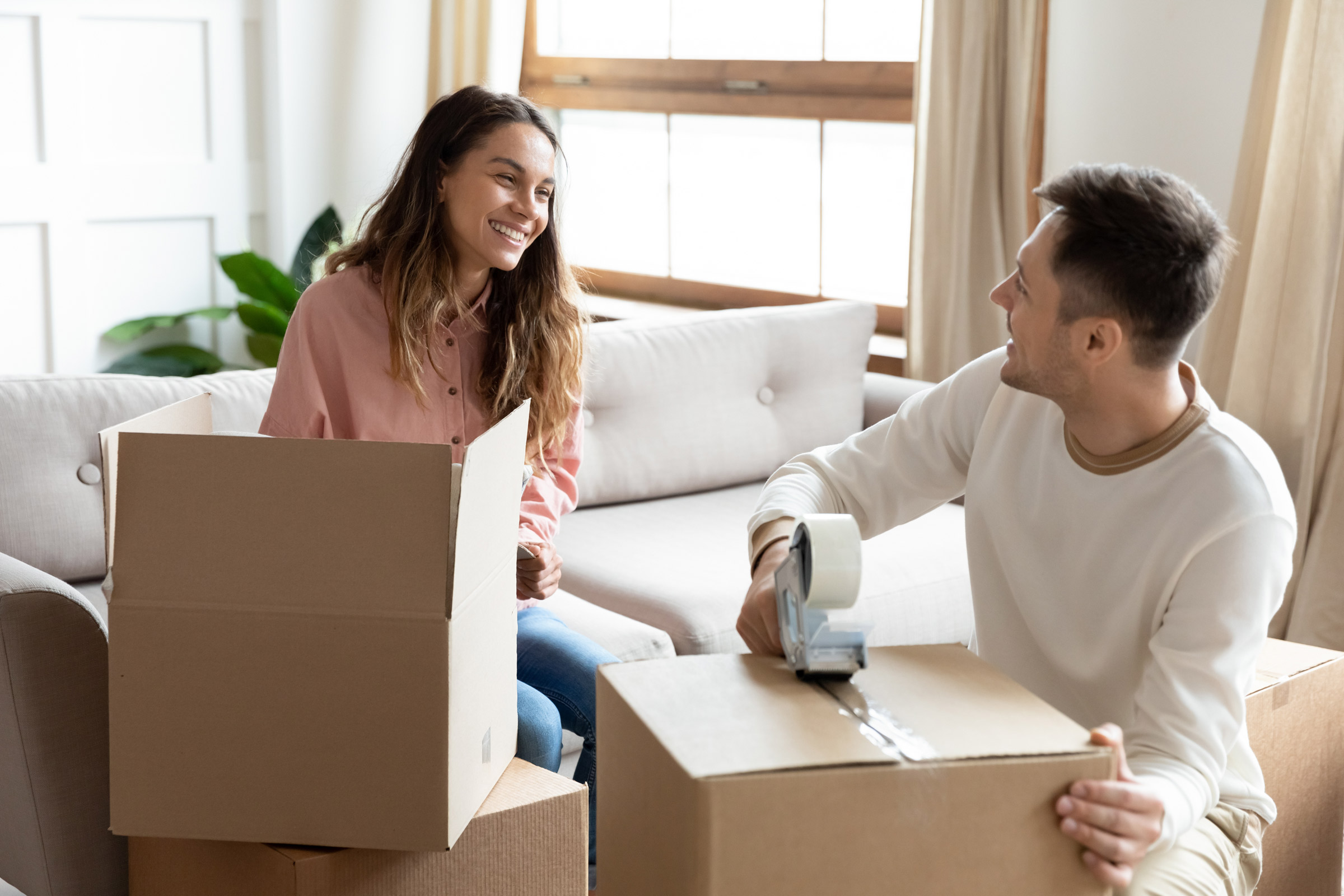 Lächelndes Paar packt Umzugskartons in heller Wohnung – gemeinsamer Umzug oder Start in neues Zuhause