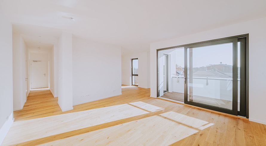 Helles Wohnzimmer mit Parkettboden, großer Fensterfront und Zugang zum Balkon – moderne Neubauwohnung