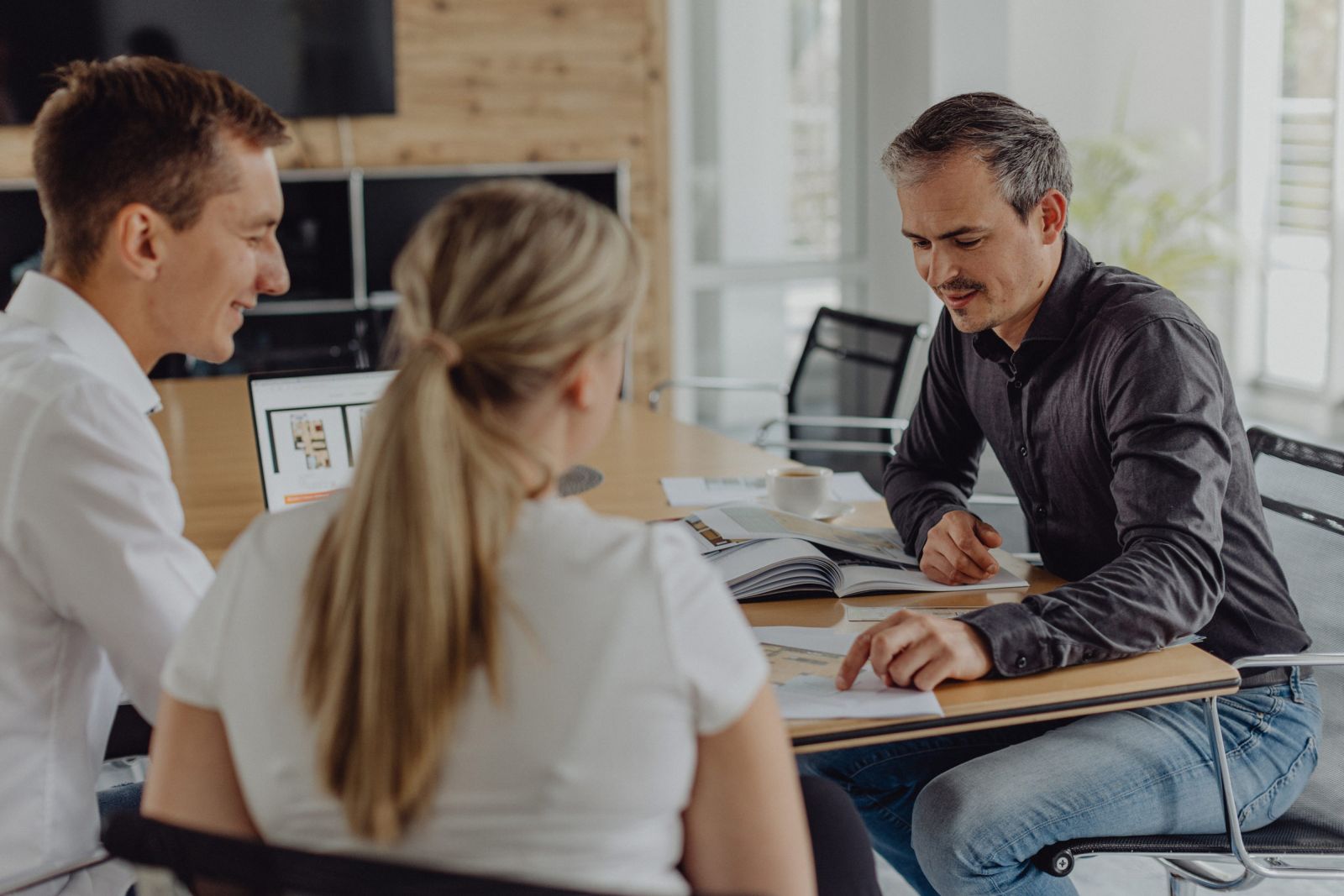 Beratungsgespräch im modernen Büro – Immobilienmakler spricht mit jungem Paar über Grundriss und Unterlagen