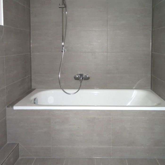 Modern gefliestes Bad mit Badewanne und Duschbrause – zeitgemäße Ausstattung in renovierter Wohnung