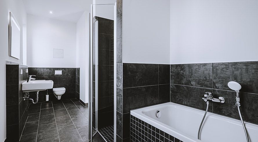 Modernes Badezimmer mit Badewanne, Dusche, WC und dunklen Fliesen – zeitgemäße Ausstattung in Neubauwohnung