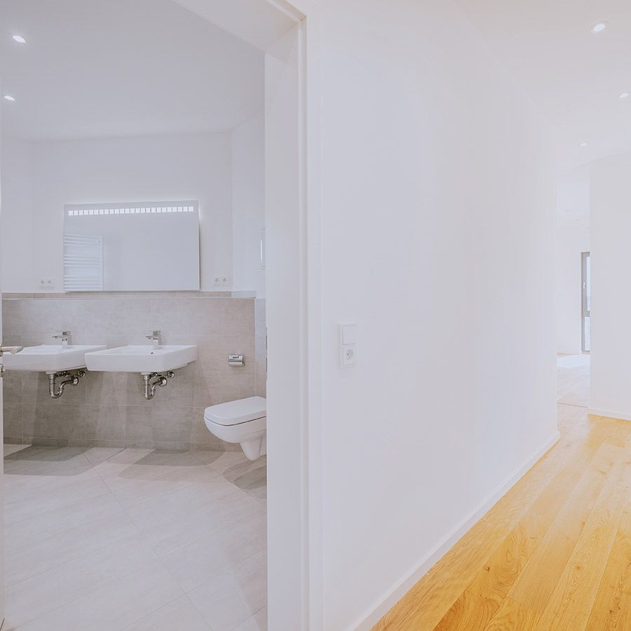 Blick vom Flur in modernes Badezimmer mit zwei Waschbecken, WC und hellen Fliesen – Neubauwohnung