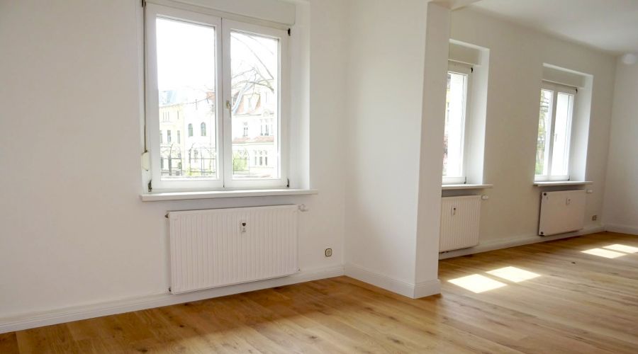 Heller Altbau-Raum mit großen Fenstern, Parkettboden und weißen Wänden – stilvolle, renovierte Wohnung
