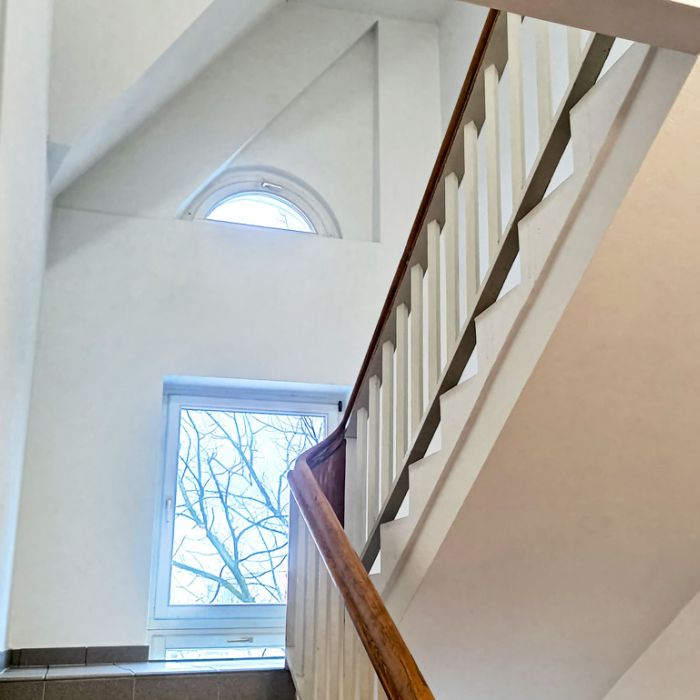 Helles Treppenhaus mit Holzhandlauf, weißem Geländer und Fenstern – gepflegter Altbau mit Tageslichteinfall