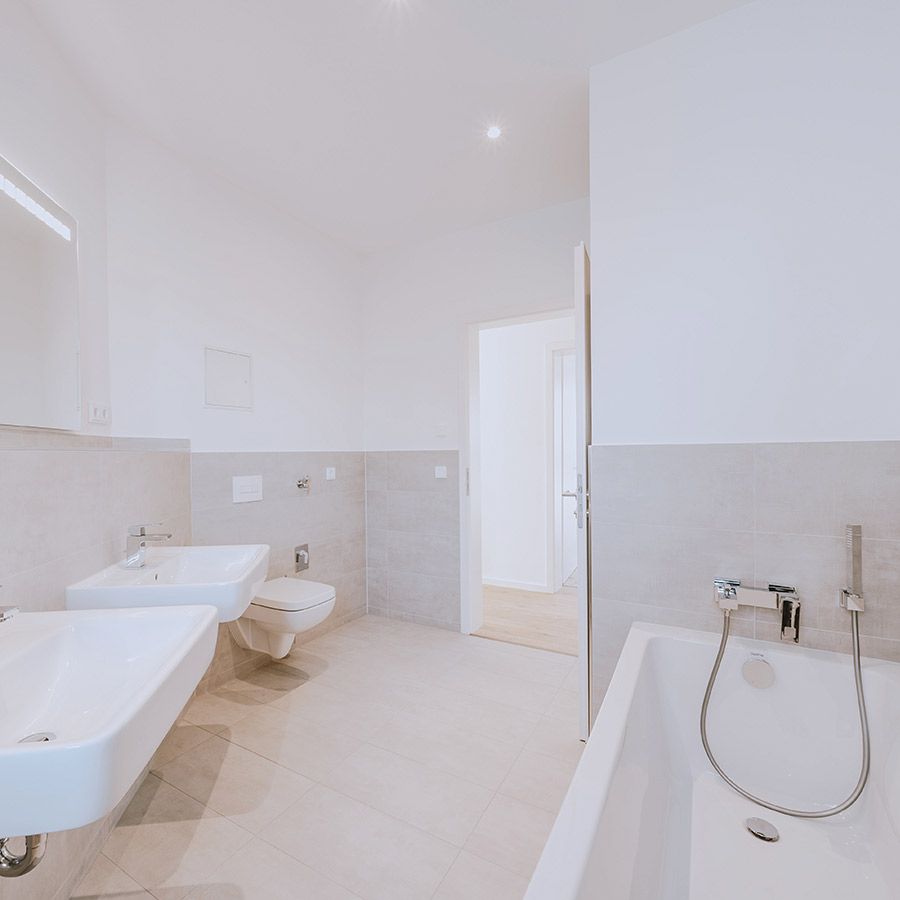 Modernes, hell gefliestes Badezimmer mit Badewanne, WC und zwei Waschbecken in einer Neubauwohnung