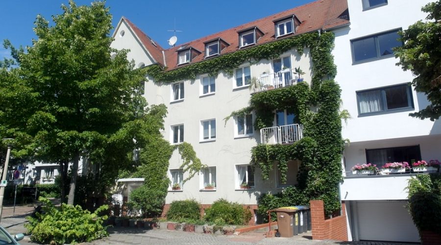 Mehrfamilienhaus mit begrünter Fassade, Balkonen und Vorgarten in ruhiger Wohngegend bei sonnigem Wetter