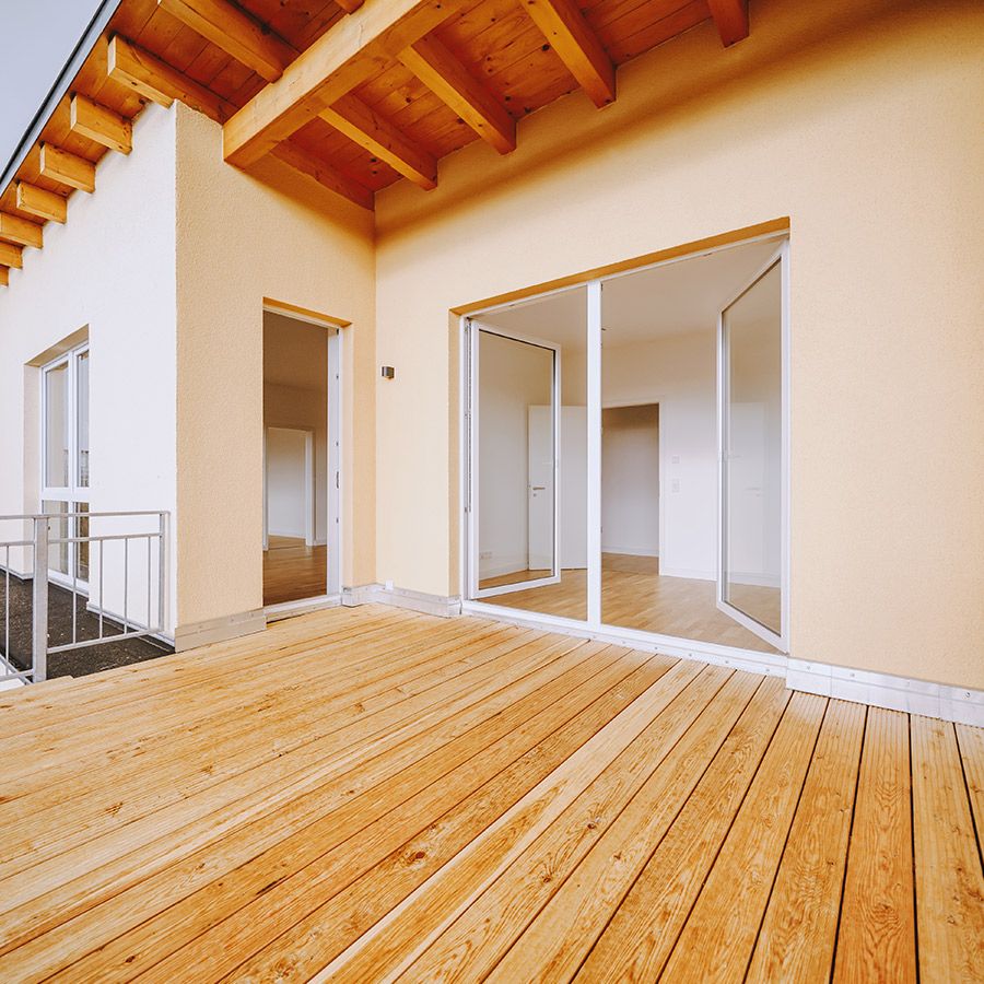 Großer überdachter Balkon mit Holzbelag und Zugang zu hellen Wohnräumen – moderne Neubauwohnung