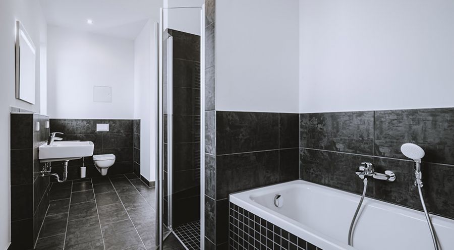 Modernes Badezimmer mit Badewanne, Dusche, WC und dunklen Fliesen – zeitgemäße Ausstattung in Neubauwohnung