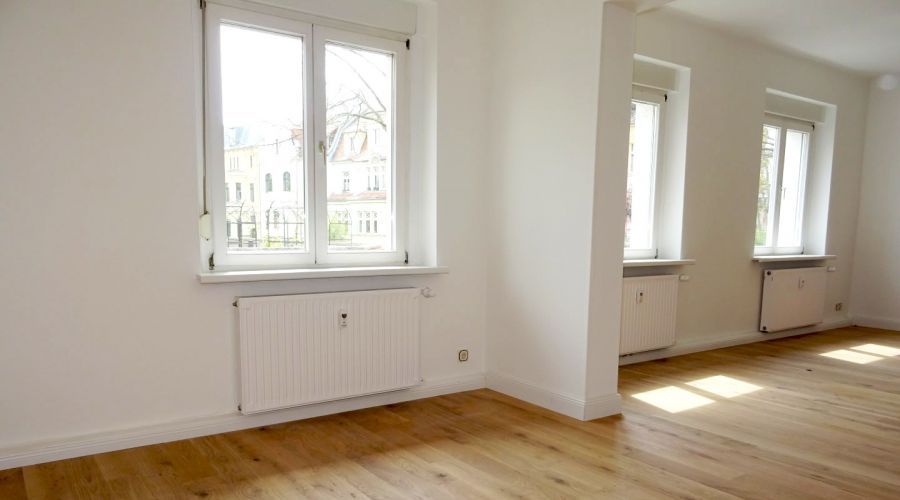 Heller Altbau-Raum mit großen Fenstern, Parkettboden und weißen Wänden – stilvolle, renovierte Wohnung