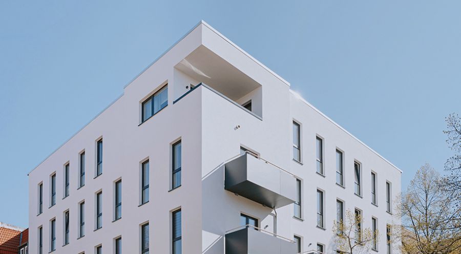 Moderne, mehrstöckige Wohnanlage mit Balkonen und klarer Architektur vor blauem Himmel – Neubau Immobilie