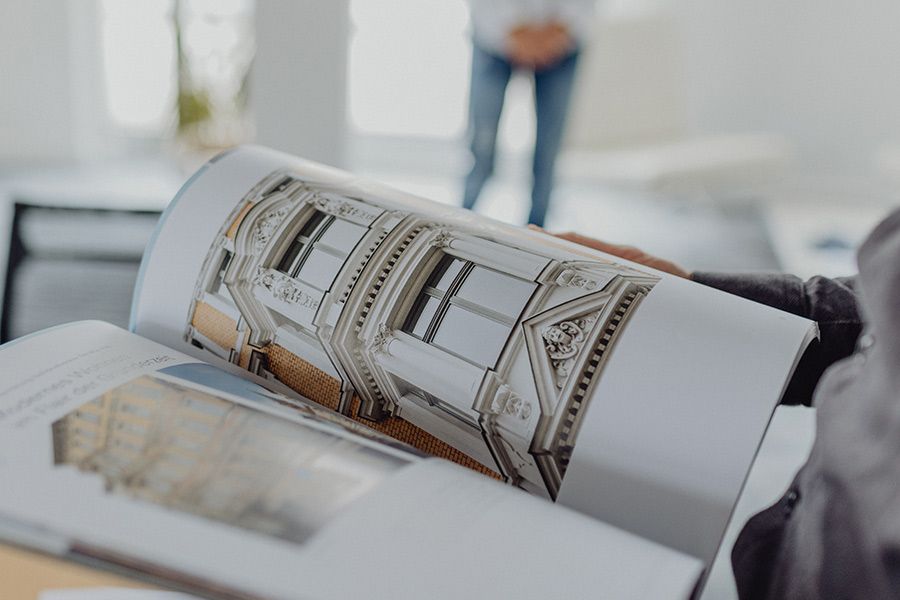 Person blättert durch Architektur-Katalog mit Foto einer Altbaufassade – Beratung oder Planung von Immobilien