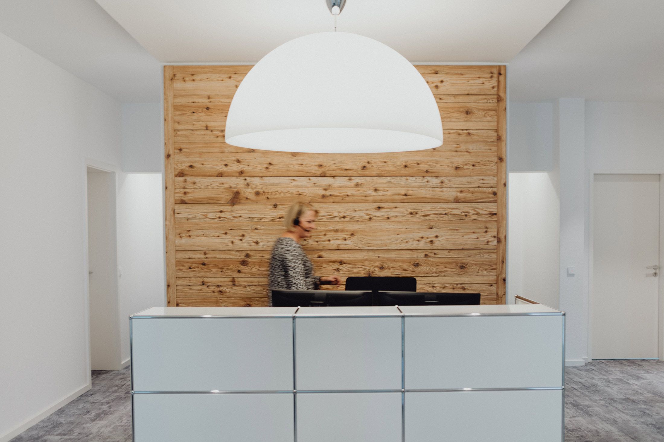 Moderne Rezeption mit Holzakzent und Mitarbeiterin mit Headset – Empfangsbereich in Büro
