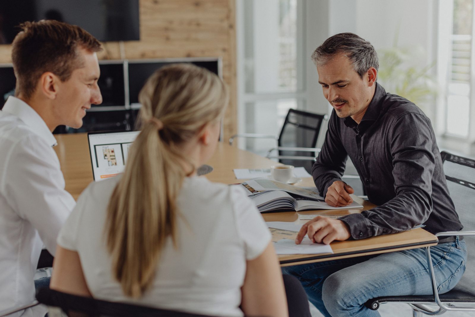 Beratungsgespräch im modernen Büro – Immobilienmakler spricht mit jungem Paar über Grundriss und Unterlagen